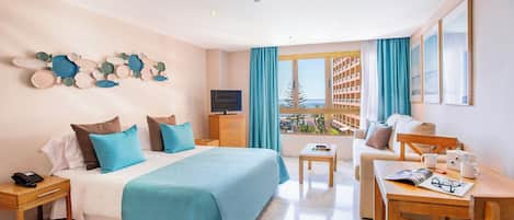 A hotel room with a bed, a TV, a desk with a chair, a window with curtains, and a balcony with a view.