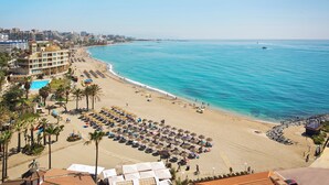 A beach with a pool, umbrellas, and a building with multiple floors. - Sunset Beach Club Hotel Apartments (Benalmádena)
