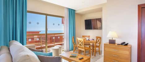 A hotel room with a balcony, a sofa, a dining table with chairs, a wooden dresser, and a TV mounted on the wall.