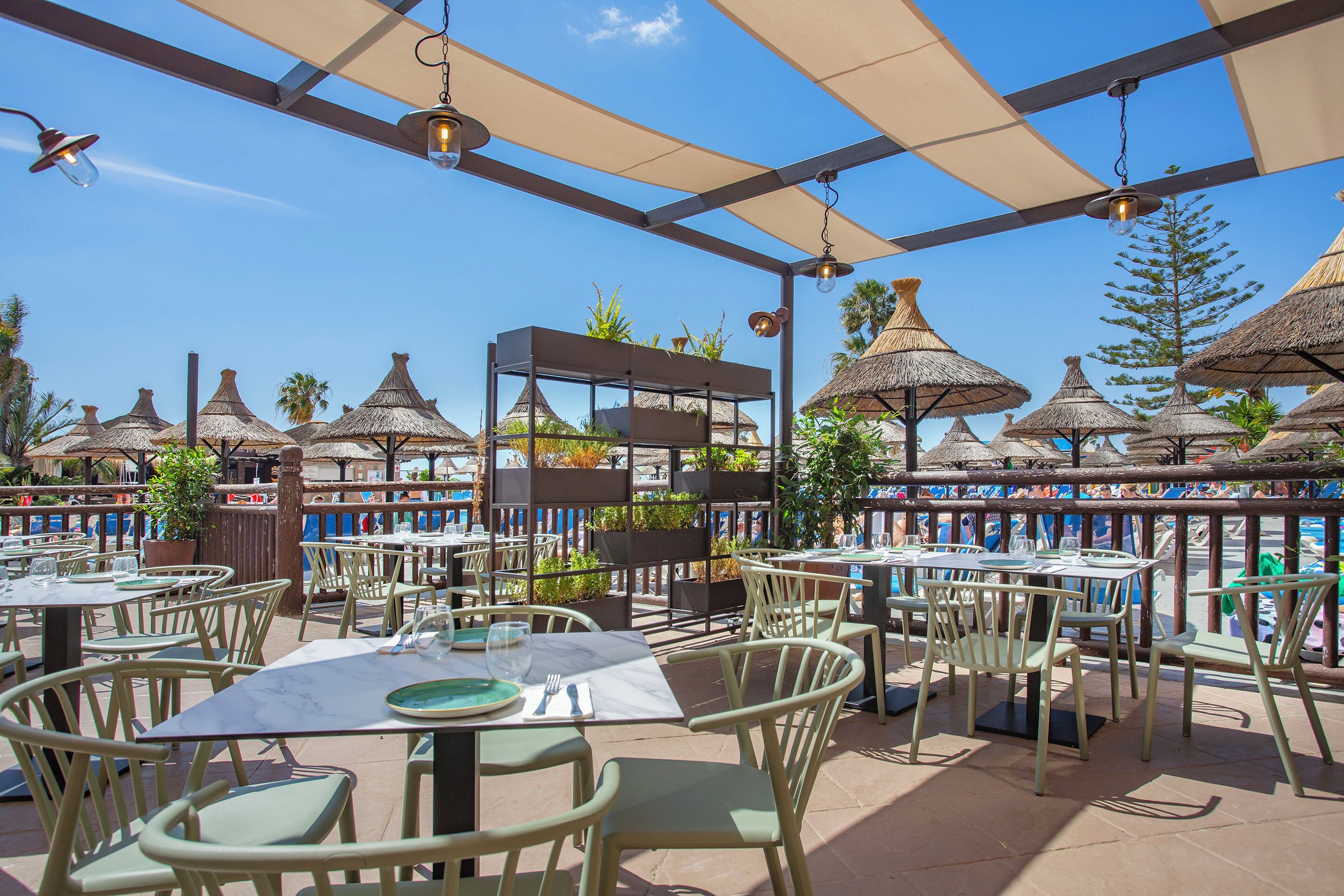 An outdoor dining area with tables and chairs, umbrellas, and a view of the sea.