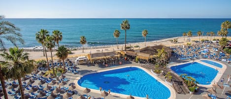 Un resort con dos piscinas grandes, palmeras y vistas a la playa.