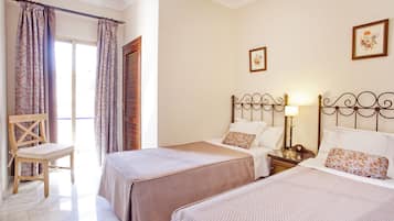 Una habitación de hotel con dos camas, una silla de madera, una mesita de noche y una lámpara.