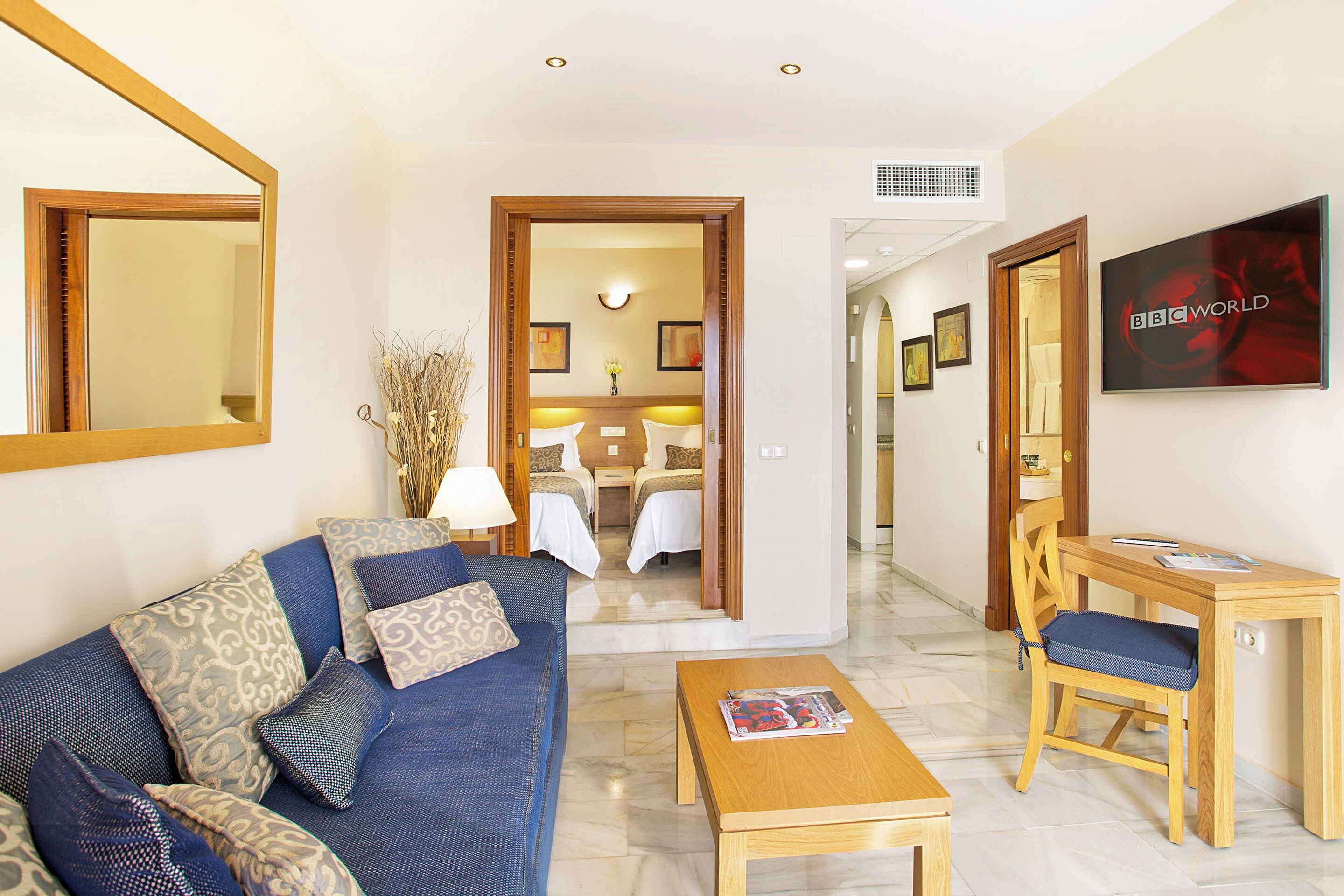 A hotel room with a sofa, a wooden coffee table, a TV, and a desk with a chair.