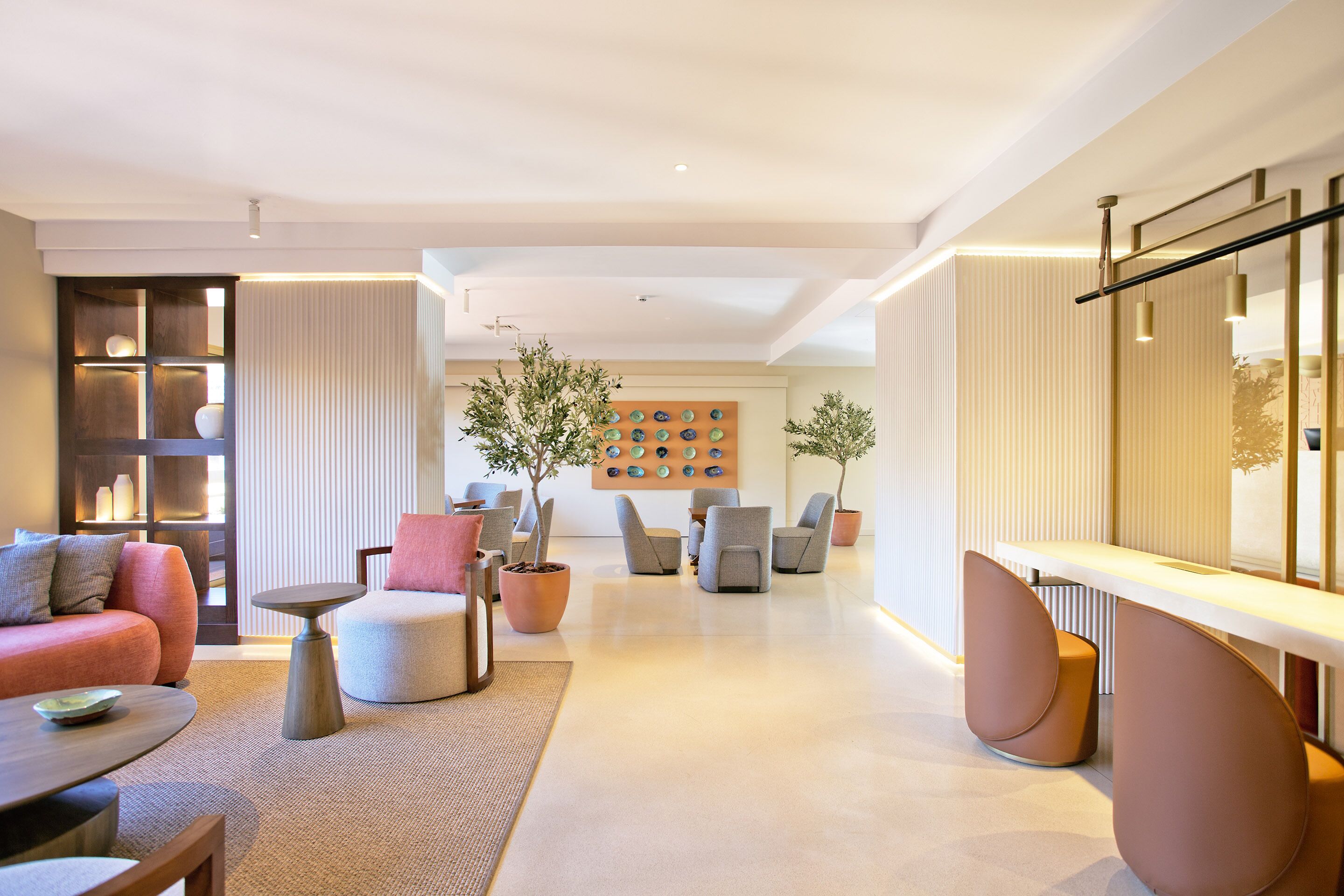 Una sala de estar moderna con un sofá, sillones, una mesa de centro y una chimenea. Hay plantas en macetas y una pared con platos decorativos.
