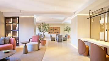 Un salon moderne avec un canapé, des fauteuils, une table basse et une cheminée. On y trouve des plantes en pot et un mur décoré d’assiettes.