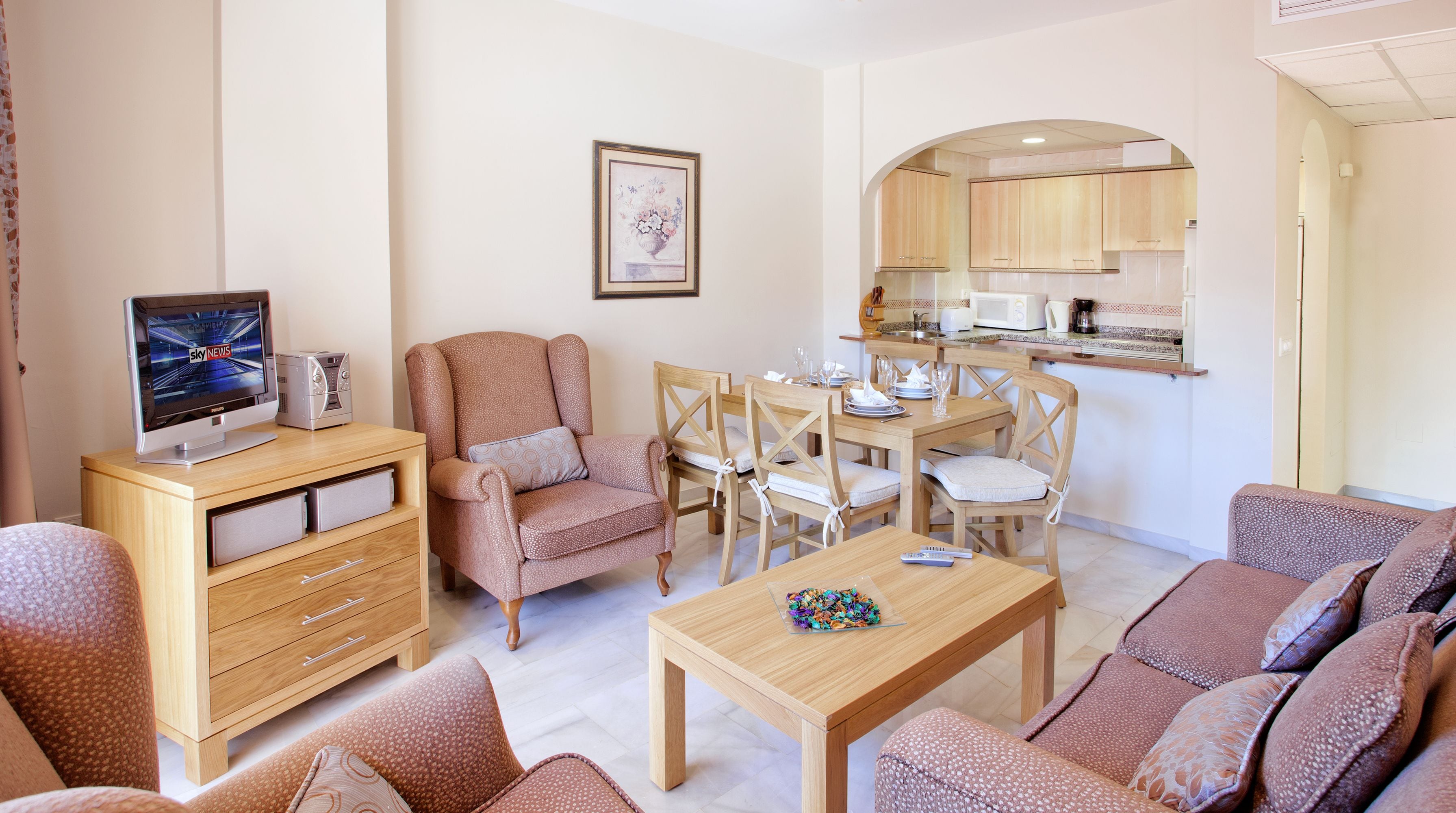 A living room with a TV, a wooden cabinet, a sofa, a coffee table, and a dining area with chairs and a table.