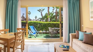 A hotel room with a sliding glass door to a patio, a wooden dining table, a sofa, and a remote control on a coffee table. - Sunset Beach Club Hotel Apartments (Benalmádena)