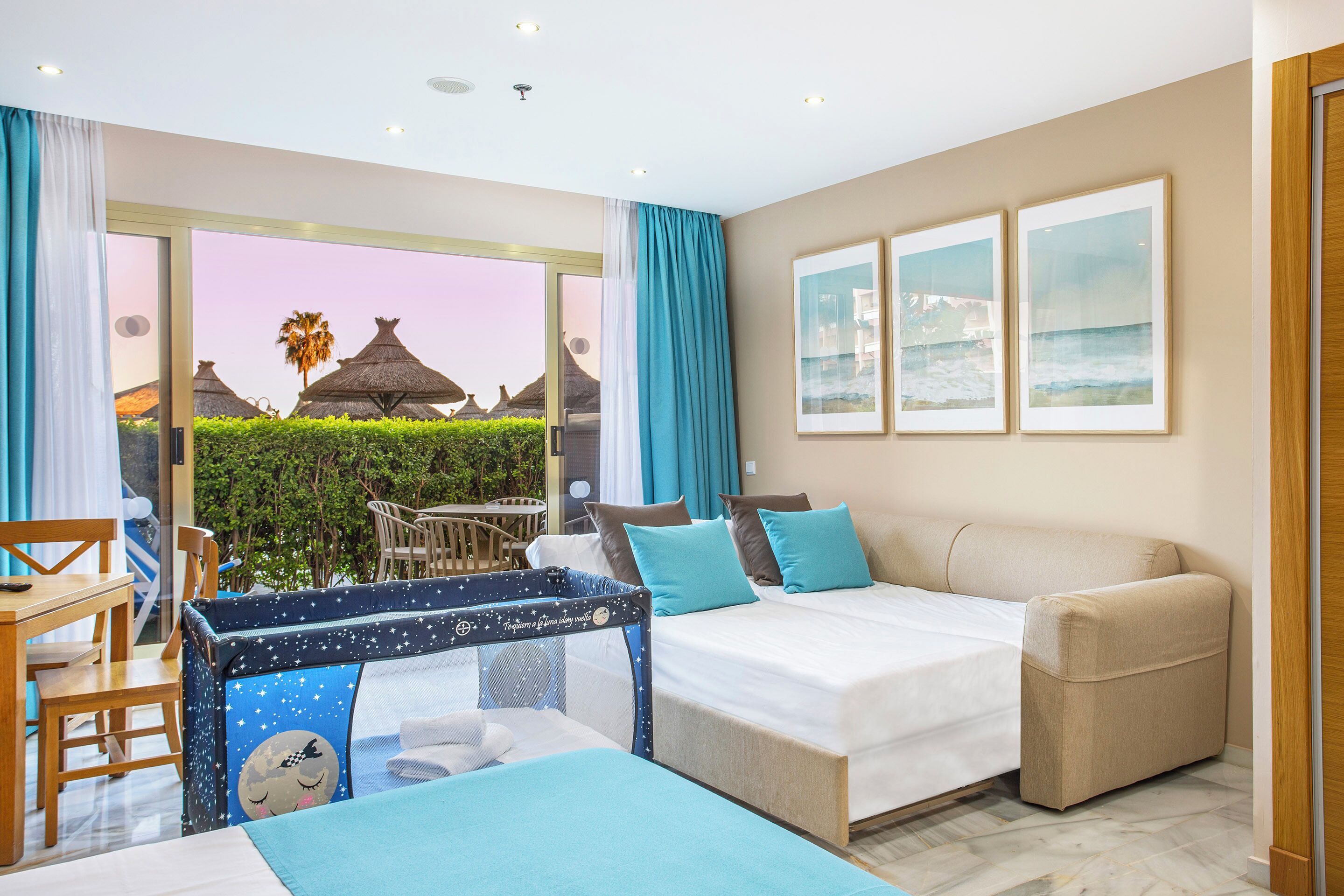 A hotel room with a bed, a sofa, a desk, and a view of the beach.
