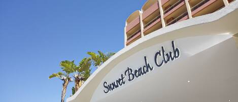 Ein Gebäude mit einem Schild, auf dem 'Sweet Beach Club' steht, und eine Palme im Vordergrund.