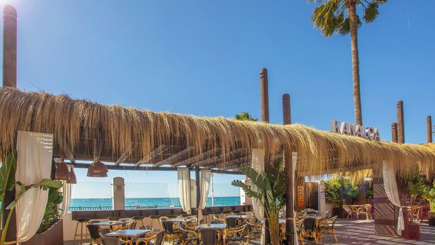 A beachside restaurant with wicker furniture, a thatched roof, and a view of the ocean. - Sunset Beach Club Hotel Apartments (Benalmádena)