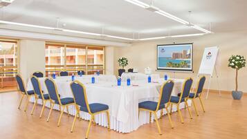 A conference room with a round table, blue chairs, white tablecloths, and a cityscape poster on the wall.