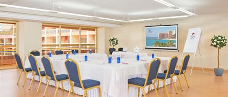 A conference room with a round table, blue chairs, white tablecloths, and a cityscape poster on the wall.