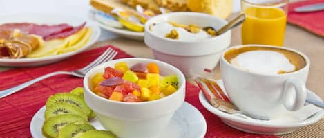 Una tavola imbandita per la colazione con una ciotola di frutta, fette di pane tostato, un bicchiere di succo d'arancia e una tazza di caffè.