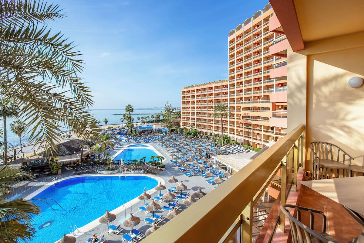 A hotel pool area with multiple lounge chairs and umbrellas, a large pool, and a view of the ocean.