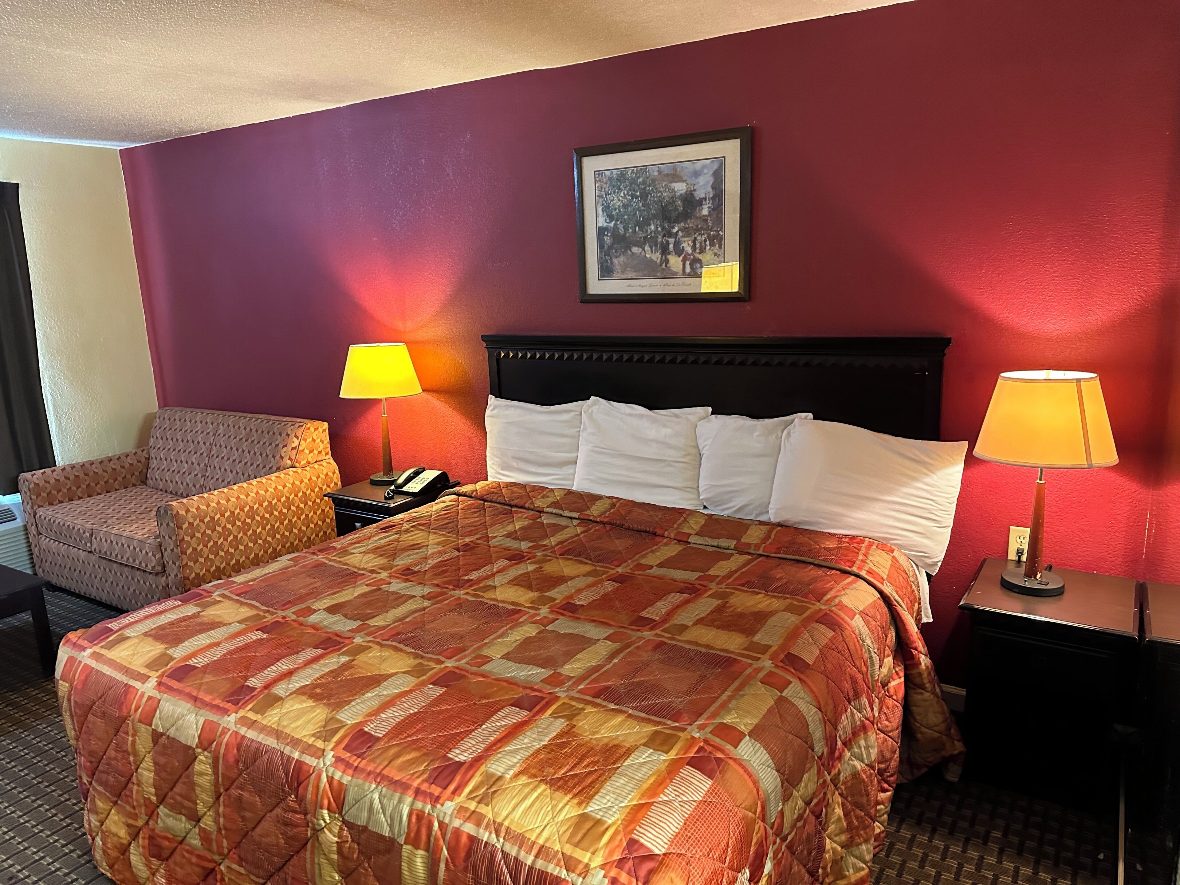 A hotel room with a large bed, two bedside lamps, a chair, and a framed picture on the wall.