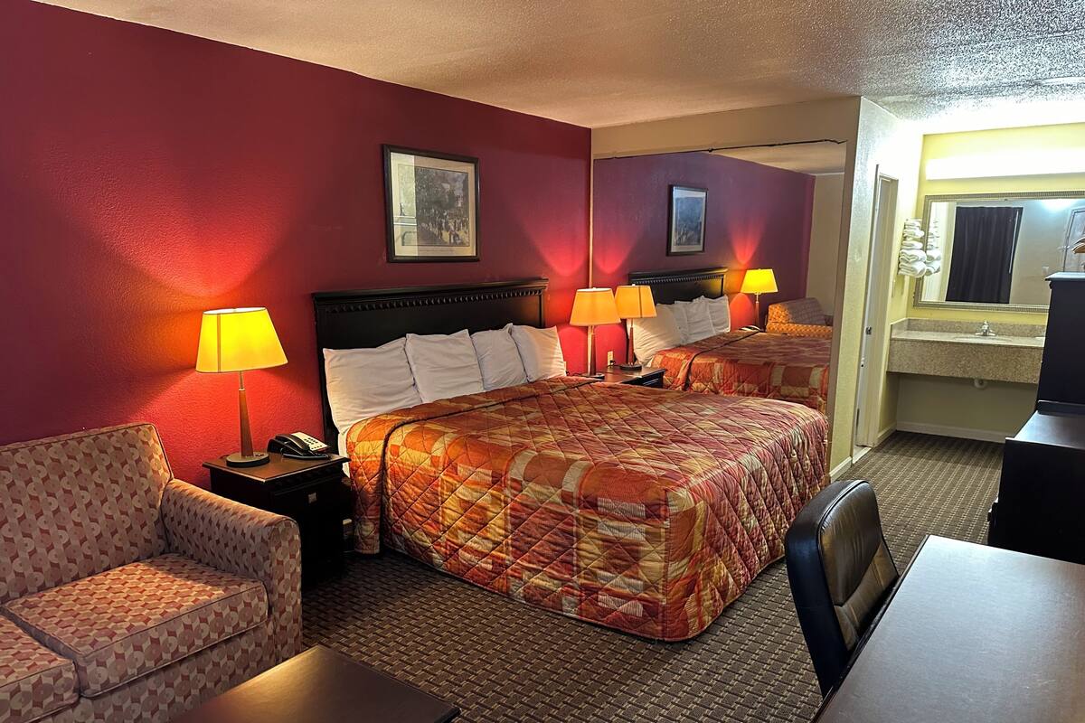 Habitación de hotel con una cama grande, dos mesitas de noche con lámparas, un sofá, un escritorio y un baño visible a través de una puerta abierta.