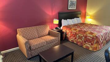 Habitación de hotel con sofá, cama con colcha, mesita de noche con lámpara y una pequeña mesa.