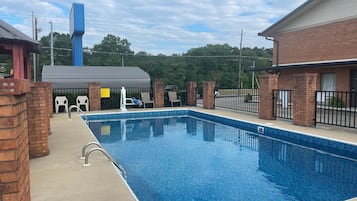 A rectangular swimming pool with a clear blue water surface, surrounded by a brick wall and a metal fence.