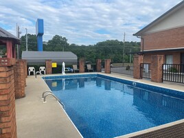 Una piscina rectangular con una superficie de agua azul cristalina, rodeada por un muro de ladrillo y una cerca metálica.