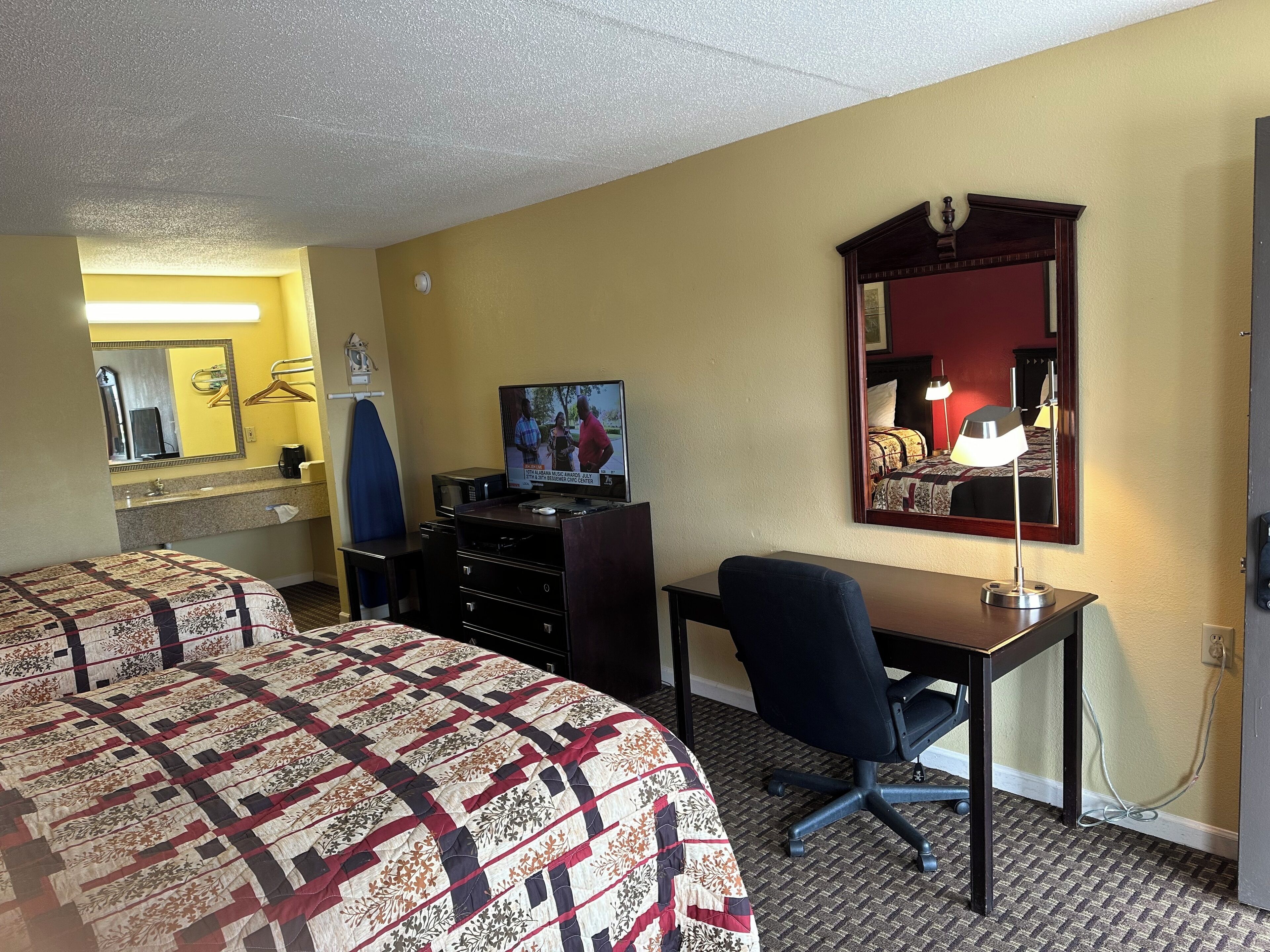 A hotel room with two beds, a desk, a chair, a television, and a mirror.