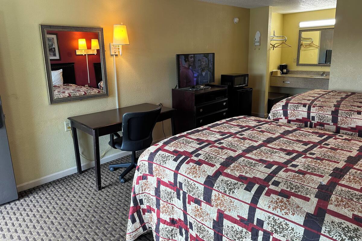 Una habitación de hotel con dos camas, un escritorio, un televisor, un espejo y una lámpara.