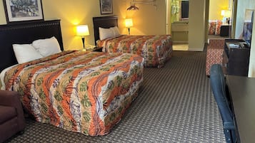 Habitación de hotel con dos camas, un escritorio, una silla, un televisor y un baño visible a través de una puerta abierta.