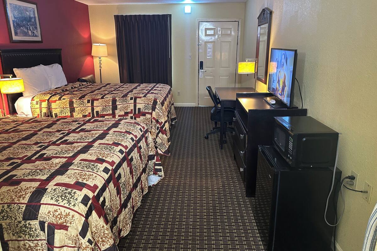 Una habitación de hotel con dos camas, un escritorio con computadora, televisión y microondas.