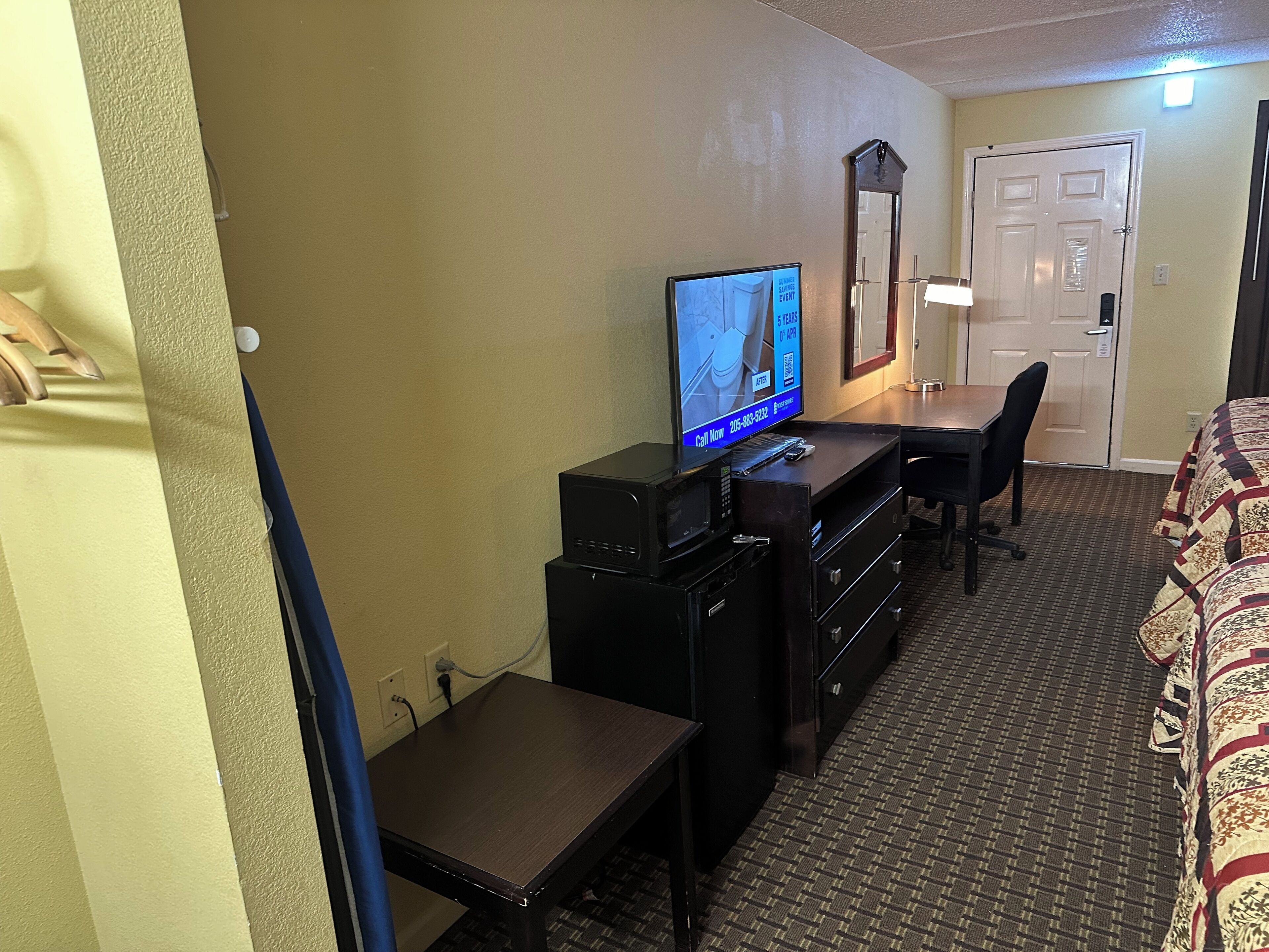 Una habitación de hotel con cama, escritorio, televisor y espejo.