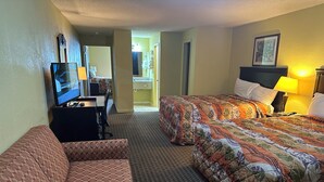 Habitación de hotel con sofá, cama con ropa de cama floral, televisor y escritorio con lámpara.