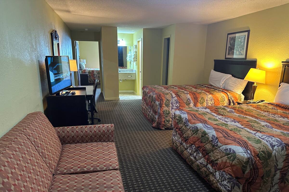 Habitación de hotel con sofá, cama con ropa de cama floral, televisor y escritorio con lámpara.