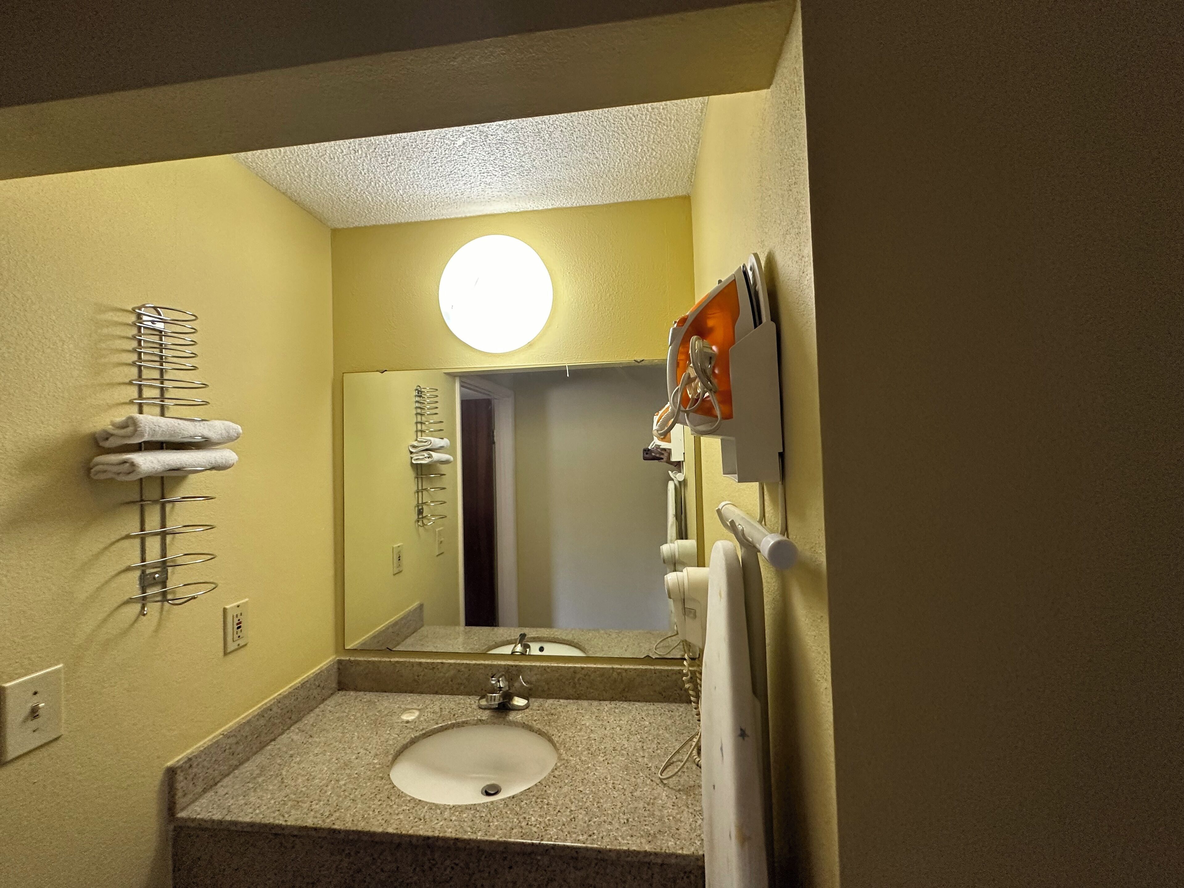 A bathroom with a sink, mirror, towel rack, and a round light fixture.