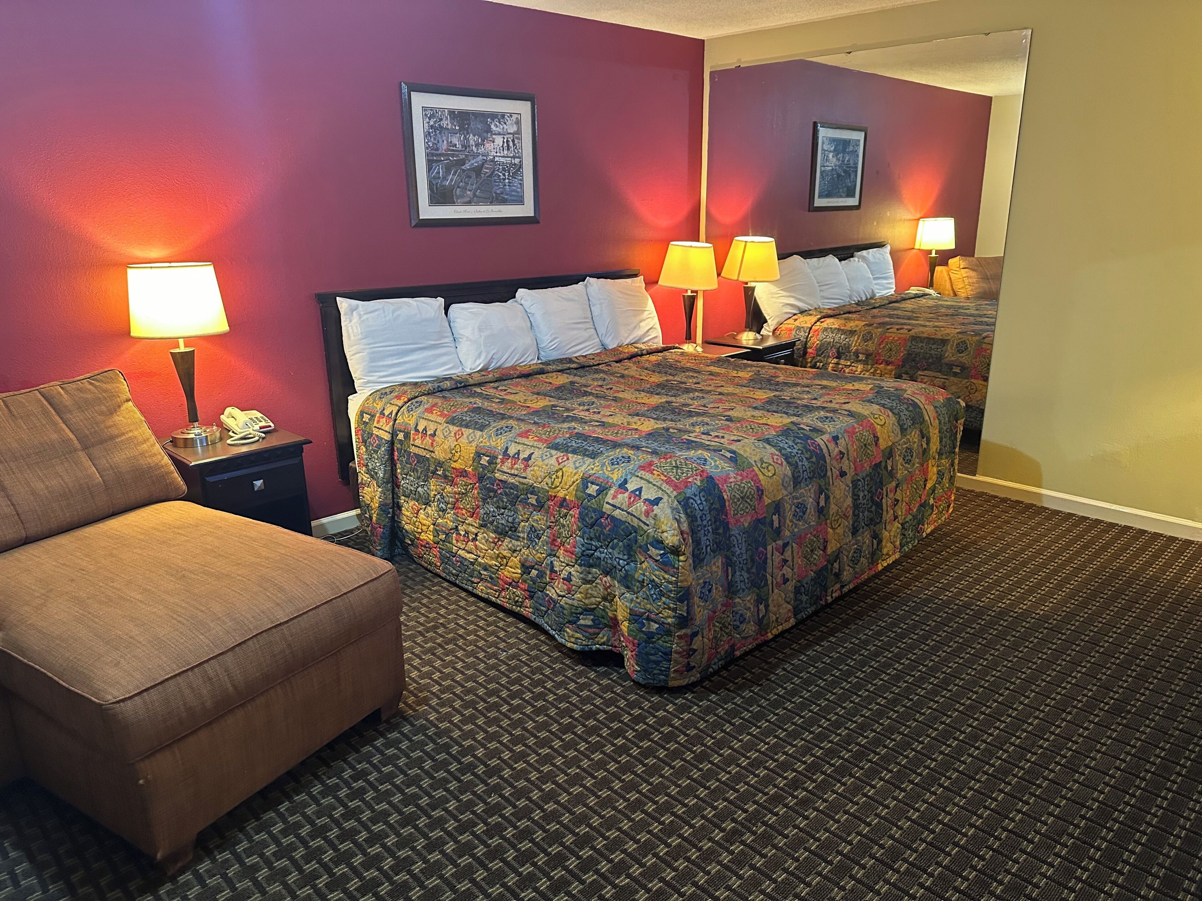 A hotel room with a bed, a chair, two bedside tables with lamps, and a large mirror.