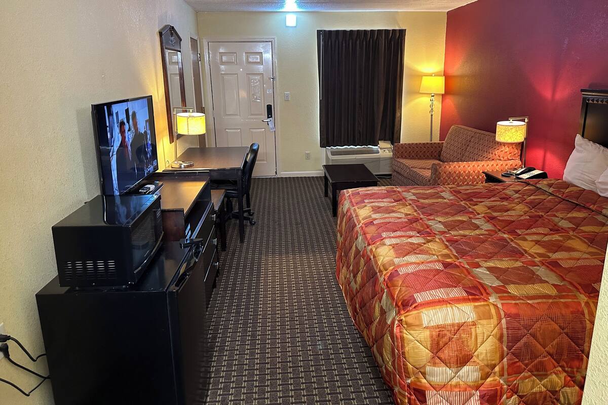 Una habitación de hotel con una cama, un escritorio con televisión, una silla, una lámpara y un teléfono.