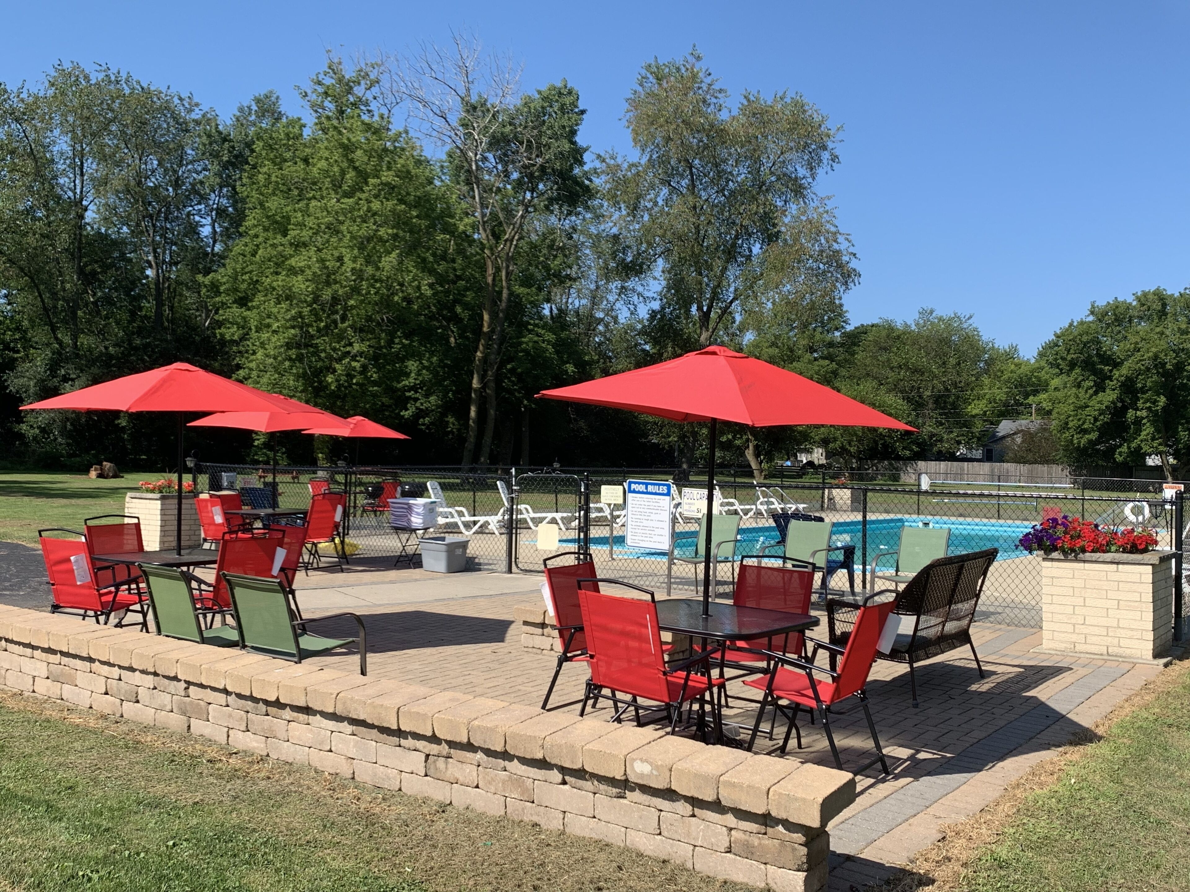 Zona de piscina con sombrillas rojas, asientos al aire libre y una piscina.