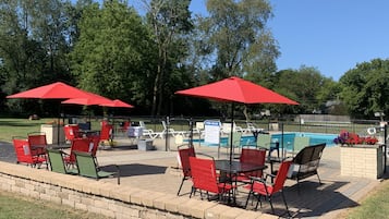 Zona de piscina con sombrillas rojas, asientos al aire libre y una piscina.