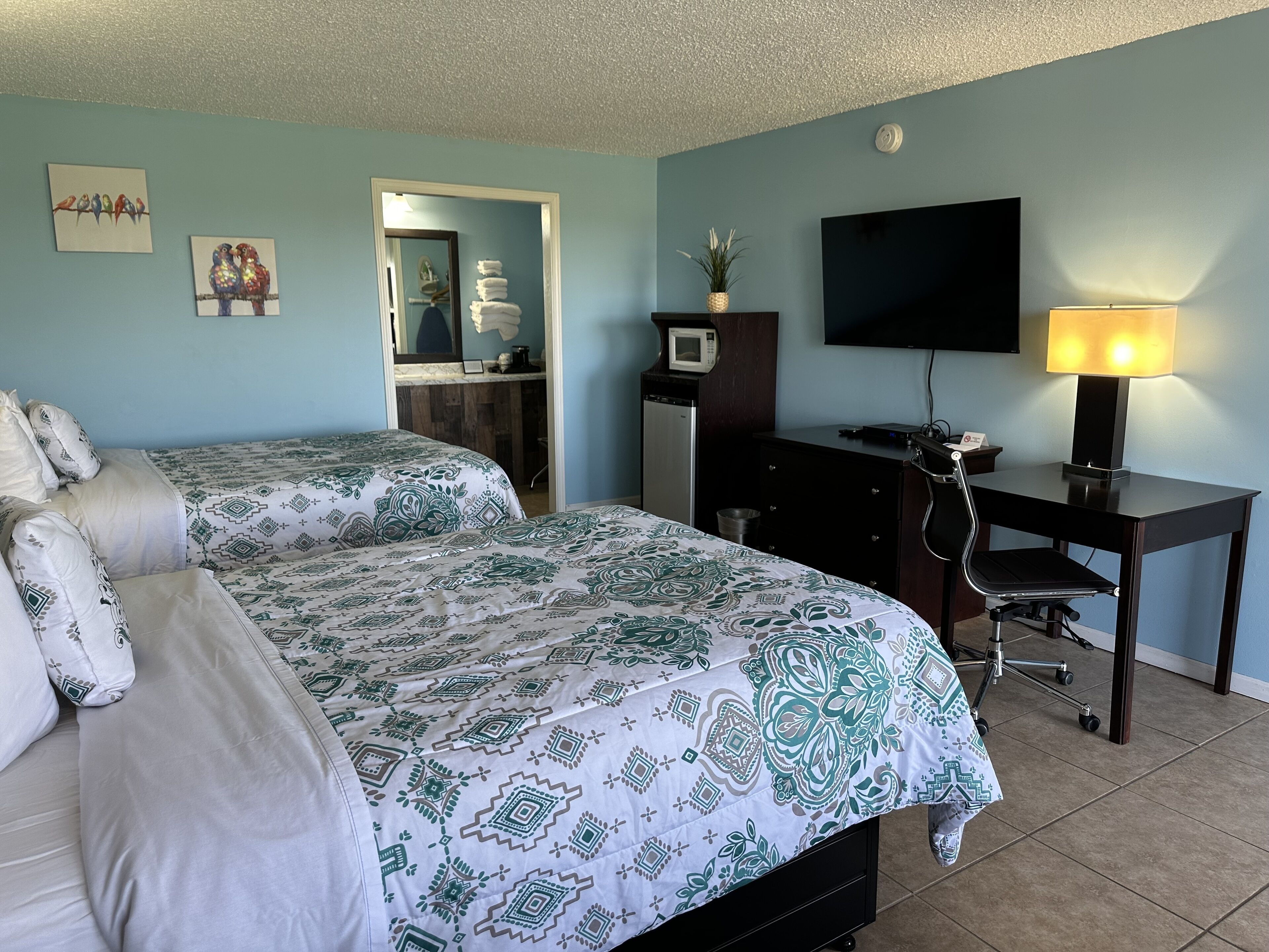 Una camera d'albergo con due letti, una scrivania, una sedia, una televisione e una lampada.