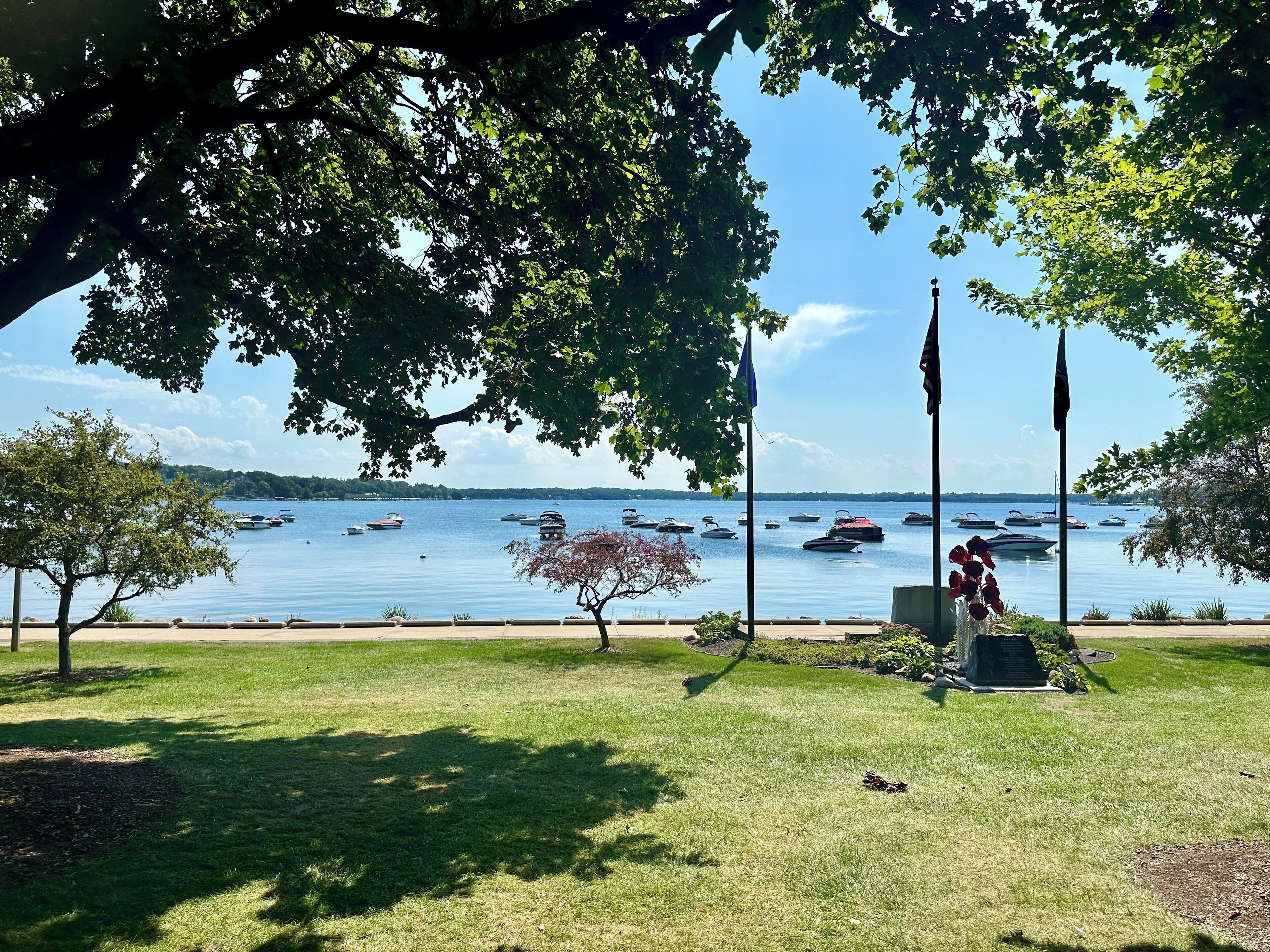 A park with a grassy area, a monument, and a view of boats on a lake.