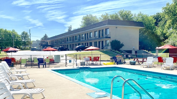 Une piscine entourée de chaises longues et de parasols, le tout délimité par une clôture, avec un bâtiment visible au loin.