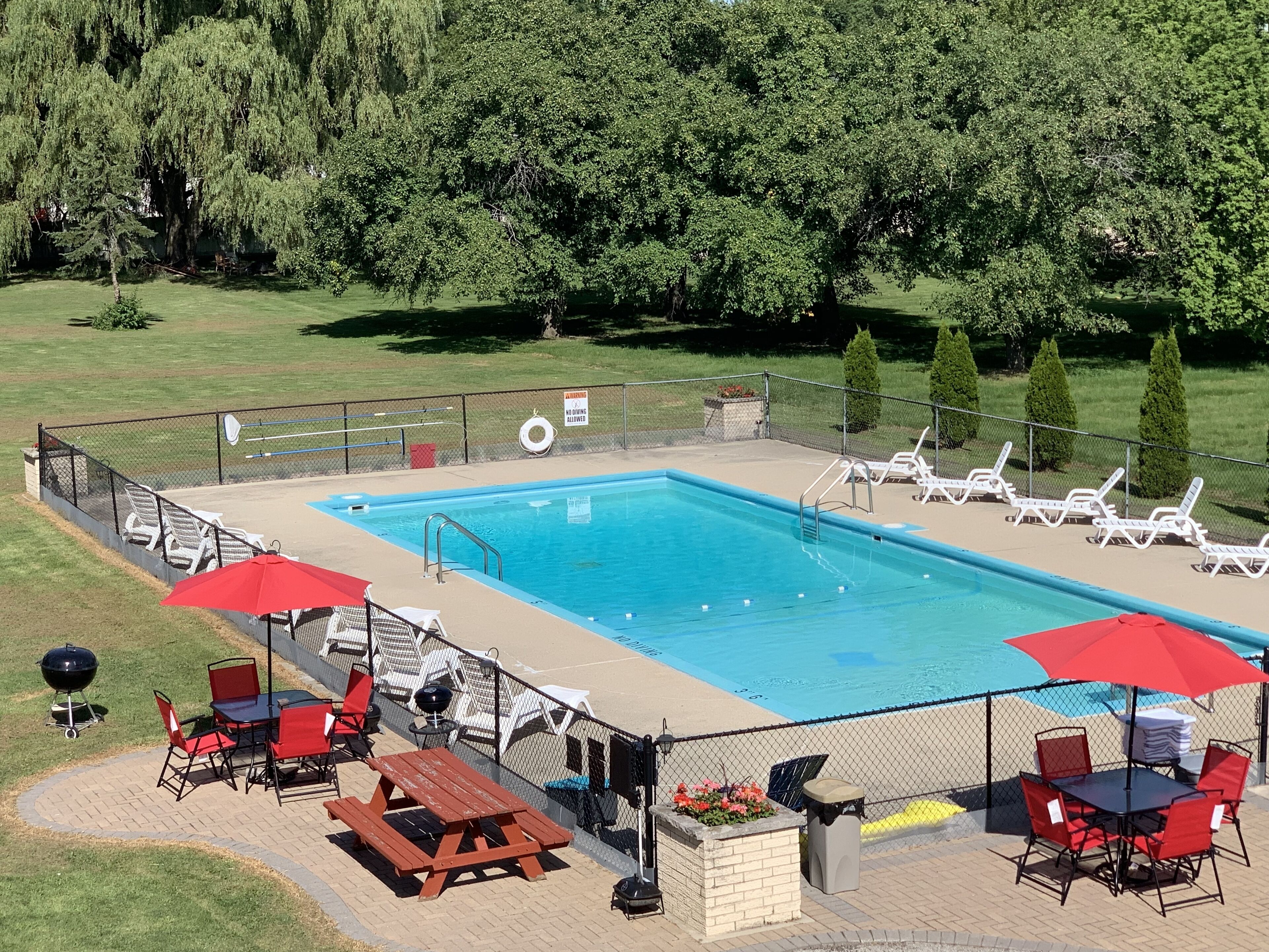 A rectangular swimming pool with a fenced deck, surrounded by lounge chairs and red umbrellas.