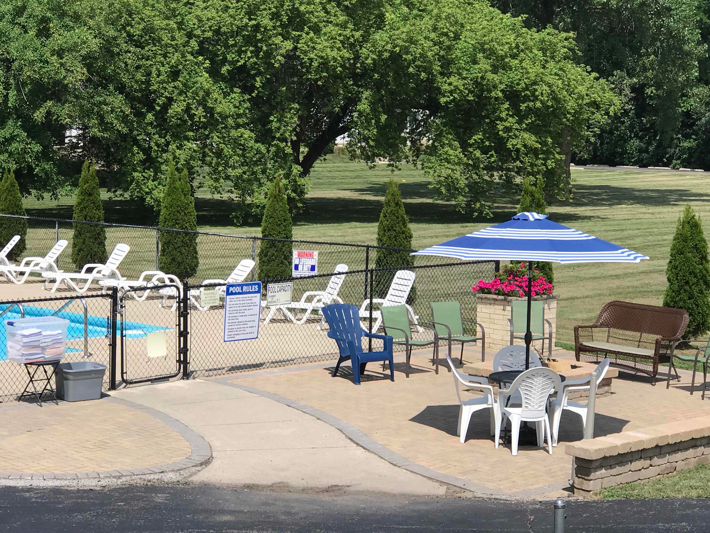 A pool area with lounge chairs, a table, and an umbrella. There are signs indicating pool rules and capacity.
