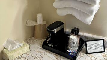 A bathroom counter with a coffee maker, a tissue box, and a stack of white towels.
