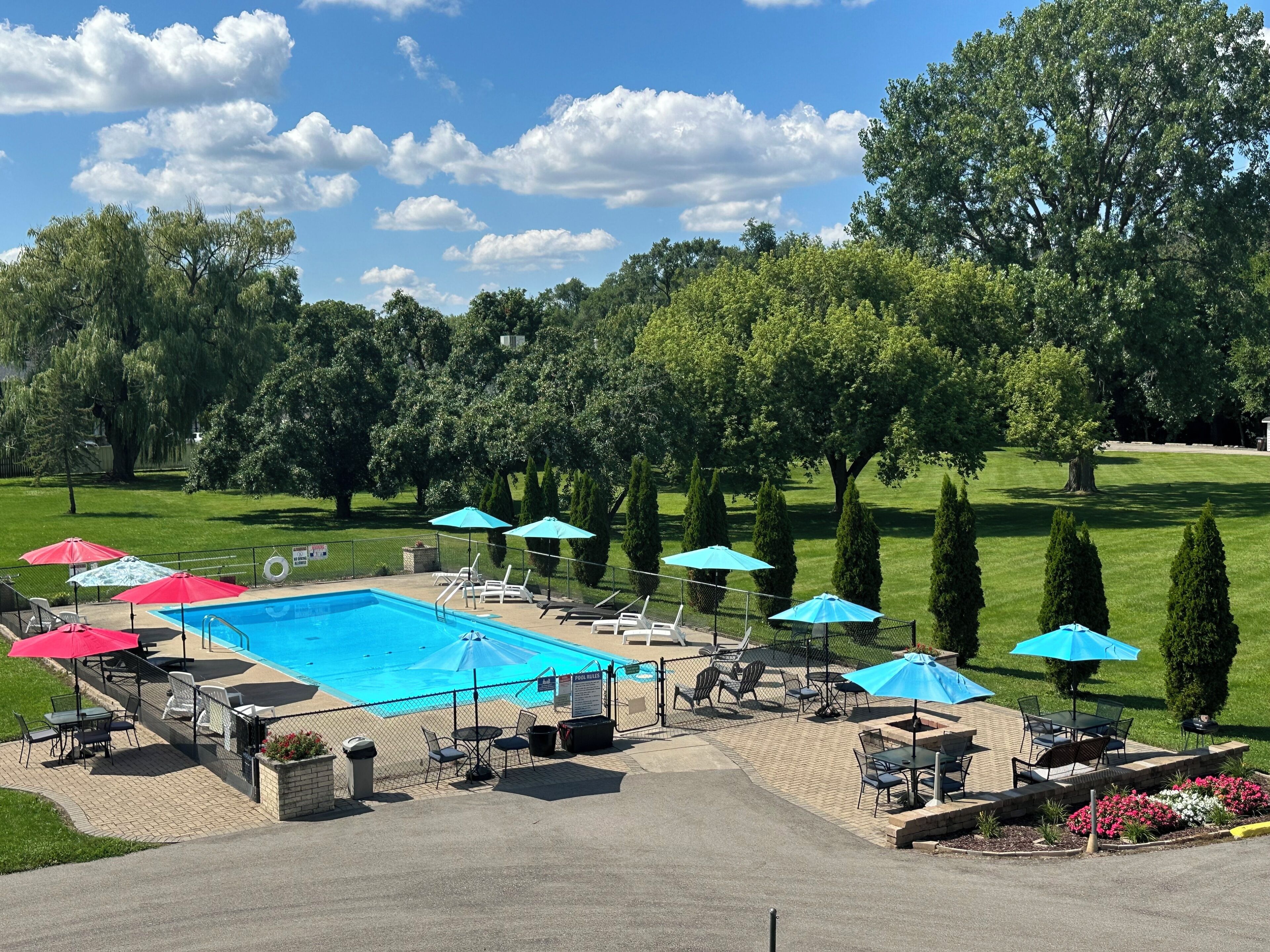 A swimming pool with lounge chairs and umbrellas, surrounded by a well-maintained lawn and trees.