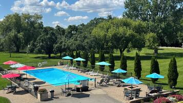 A swimming pool with lounge chairs and umbrellas, surrounded by a well-maintained lawn and trees.