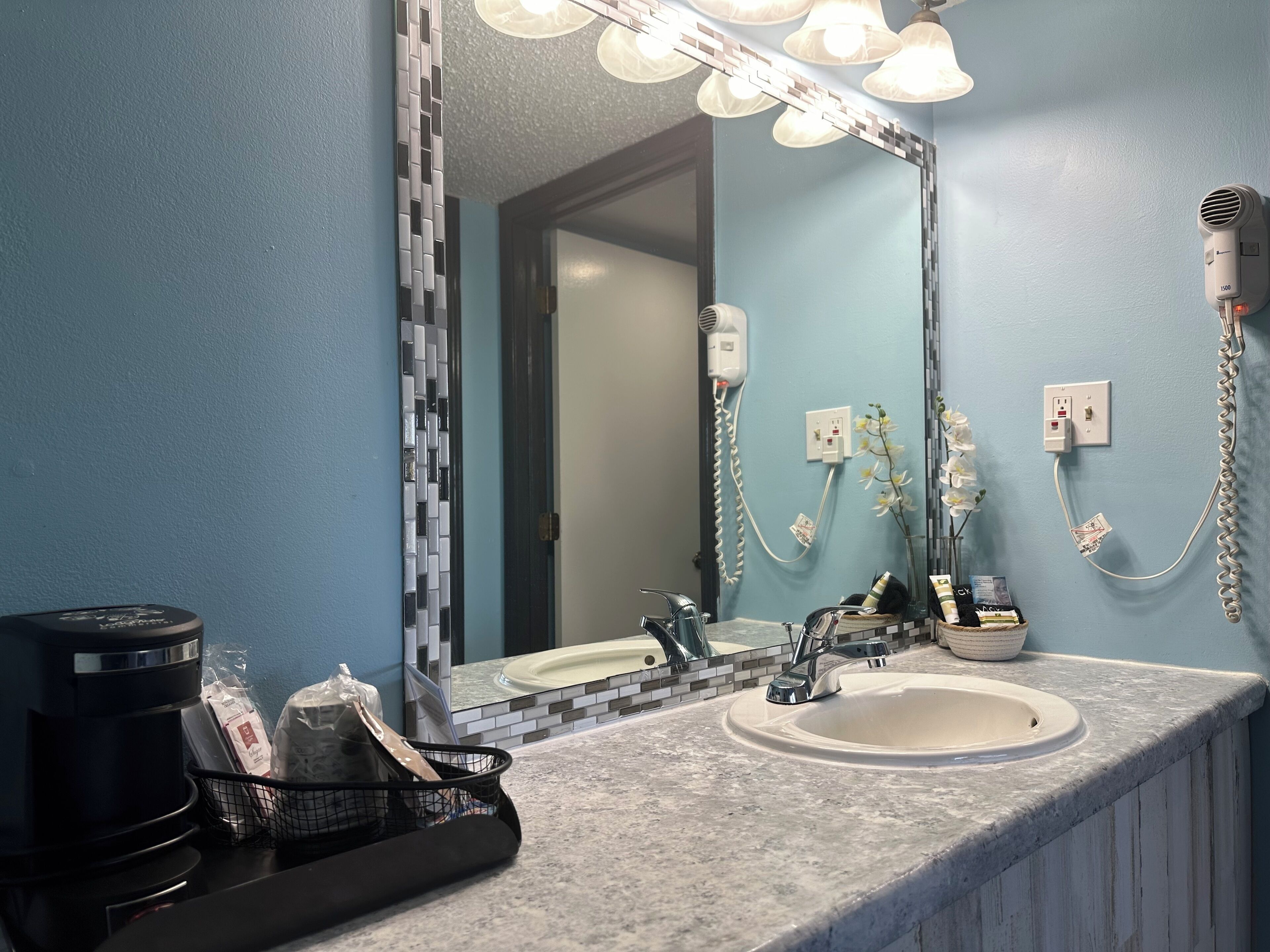 A bathroom with a sink, mirror, and hairdryer on the wall.