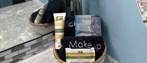 A bathroom vanity with a mirror, a white orchid plant, and a basket containing a facial bar, a tube of body lotion, and a pack of makeup wipes.