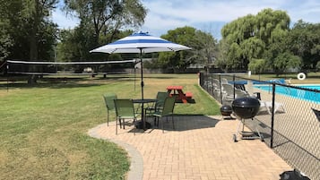 Um quintal com um alpendre de tijolos, piscina, churrasqueira e mesa de piquenique.