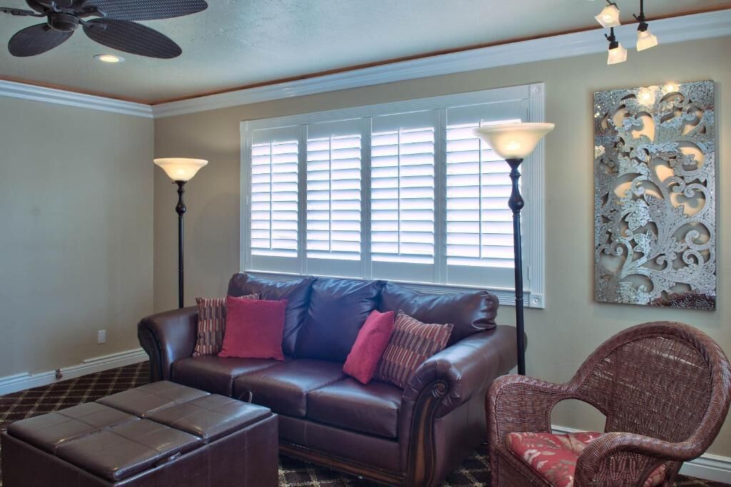 A living room with a leather sofa, a wicker chair, a floor lamp, and a decorative wall piece.