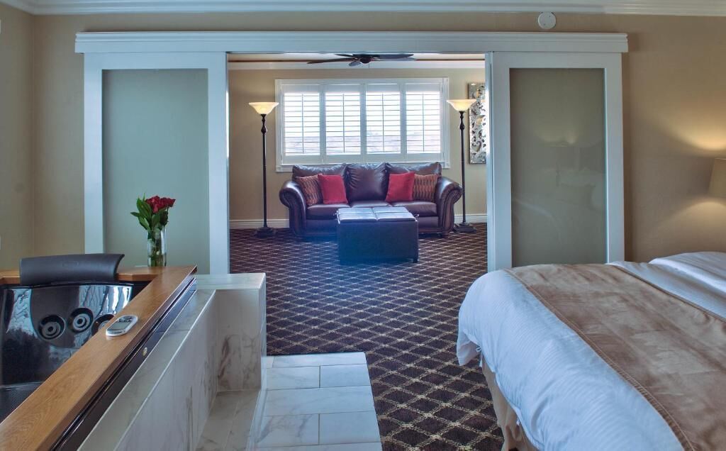Habitación de hotel con cama, escritorio con teléfono, cafetera, sofá y ventana con persianas.
