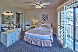 A hotel room with a large bed, a dresser, a ceiling fan, a window with blinds, and a view of the outdoors.