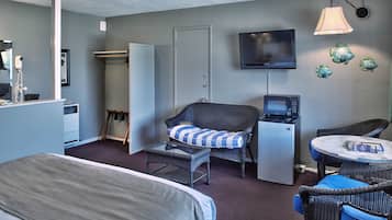 A compact hotel room with a bed, a small table, a chair, a microwave, a television, and a ceiling fan.